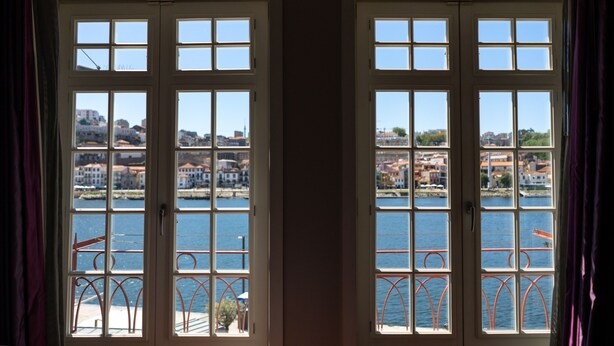 A view through a window with a metal railing, overlooking a body of water and buildings. - Guest House Douro (Porto)