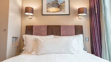 A hotel room with a bed, two wall-mounted lamps, a framed picture on the wall, and a window with curtains.