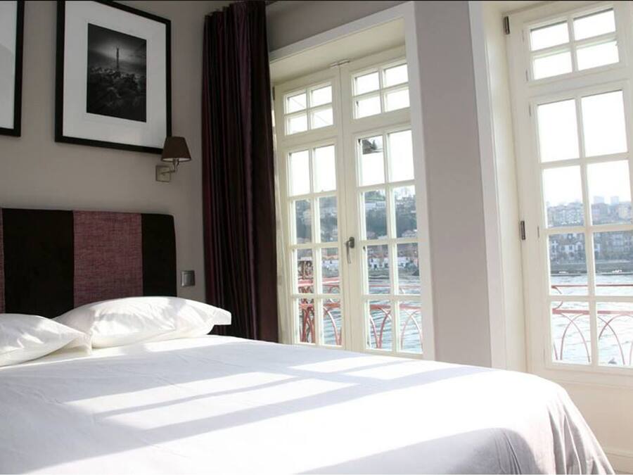 Una habitación de hotel con cama, ventana grande y vista a la ciudad.