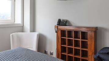 A hotel room with a bed, a chair, a television mounted on the wall, and a wooden cabinet with a telephone.