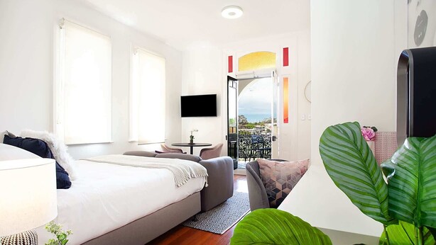 A modern bedroom with a bed, a sofa, a TV, and a balcony with a view.