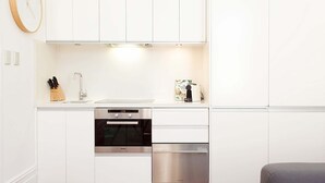A modern kitchen with white cabinetry, a built-in oven, a dishwasher, and a clock on the wall.