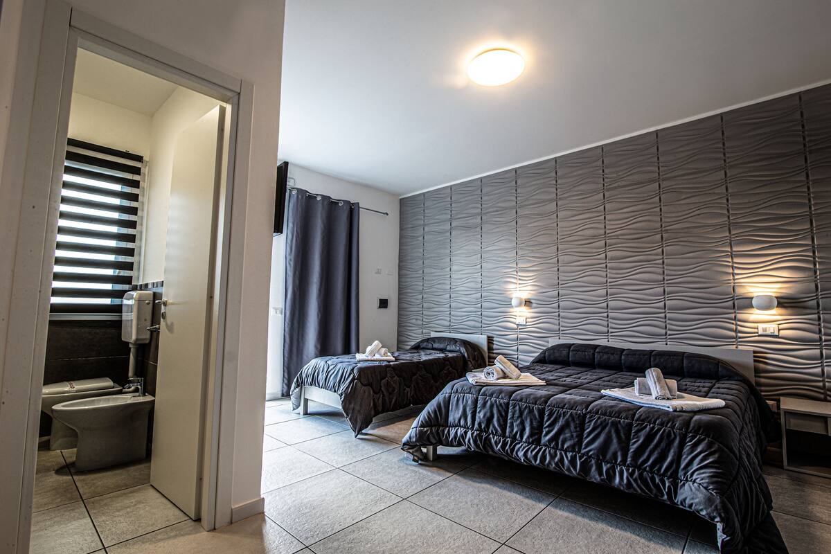 Une chambre d’hôtel moderne avec deux lits, une salle de bain et un décor mural original aux textures variées.