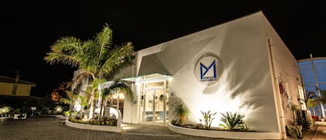 Un hotel moderno con un logotipo destacado en la fachada, una entrada bien iluminada y un camino de entrada pavimentado.
