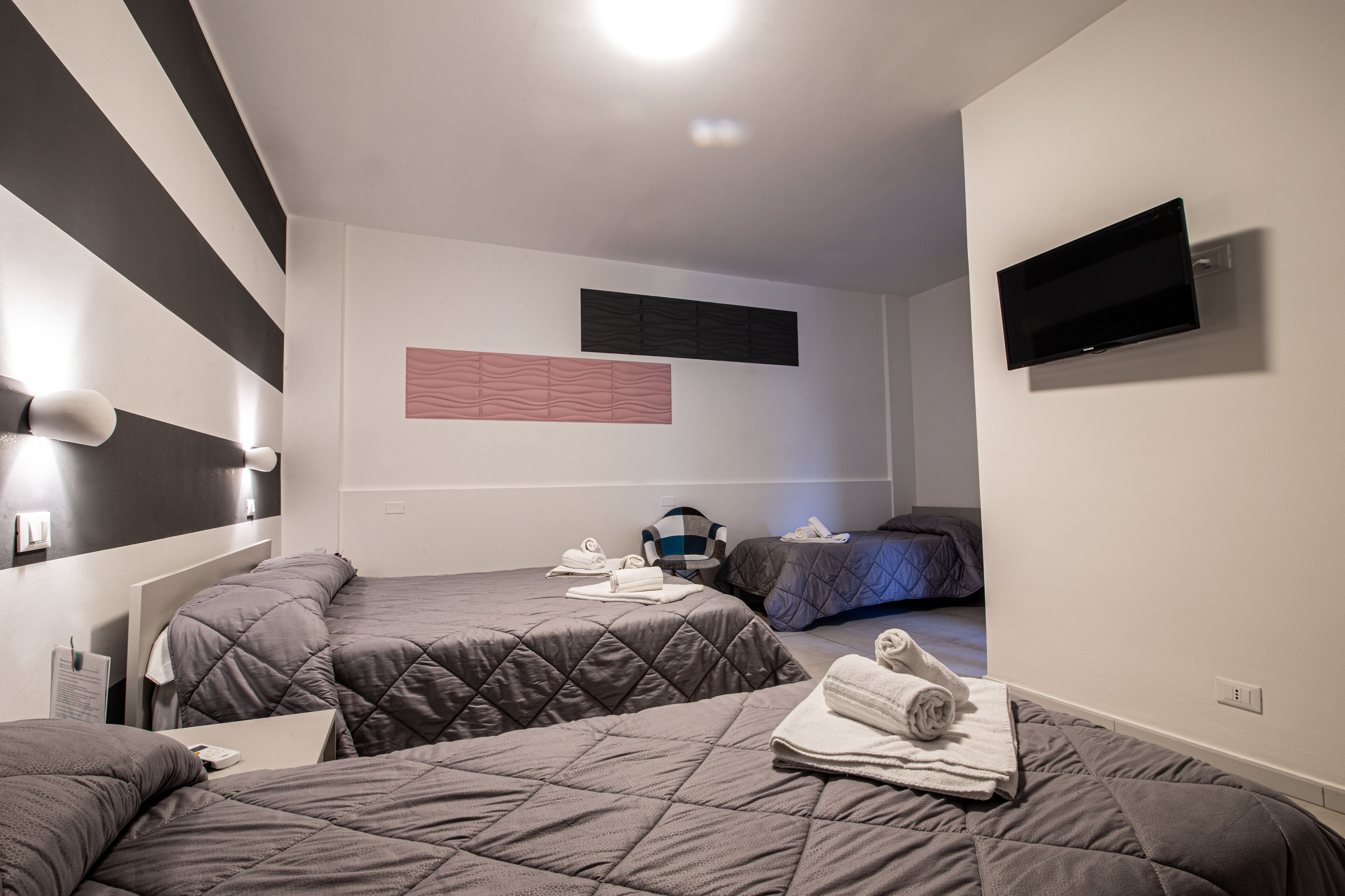 Une chambre d’hôtel avec deux lits, un téléviseur à écran plat et un luminaire fixé au mur.