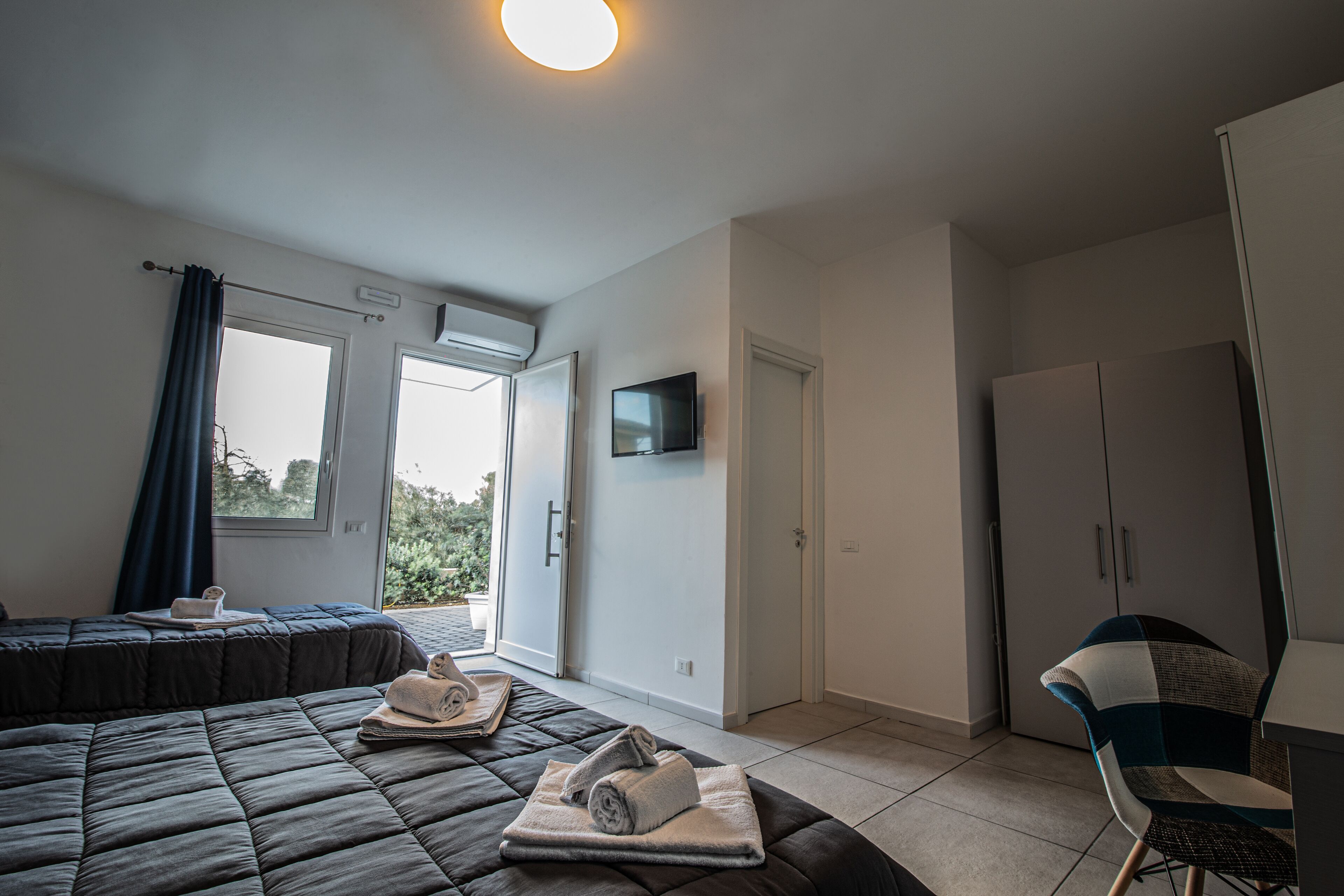 A modern hotel room with a bed, a TV, a wardrobe, and a view of the outdoors.