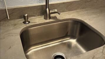 A stainless steel kitchen sink with a modern faucet, a marble countertop, and a visible drain.