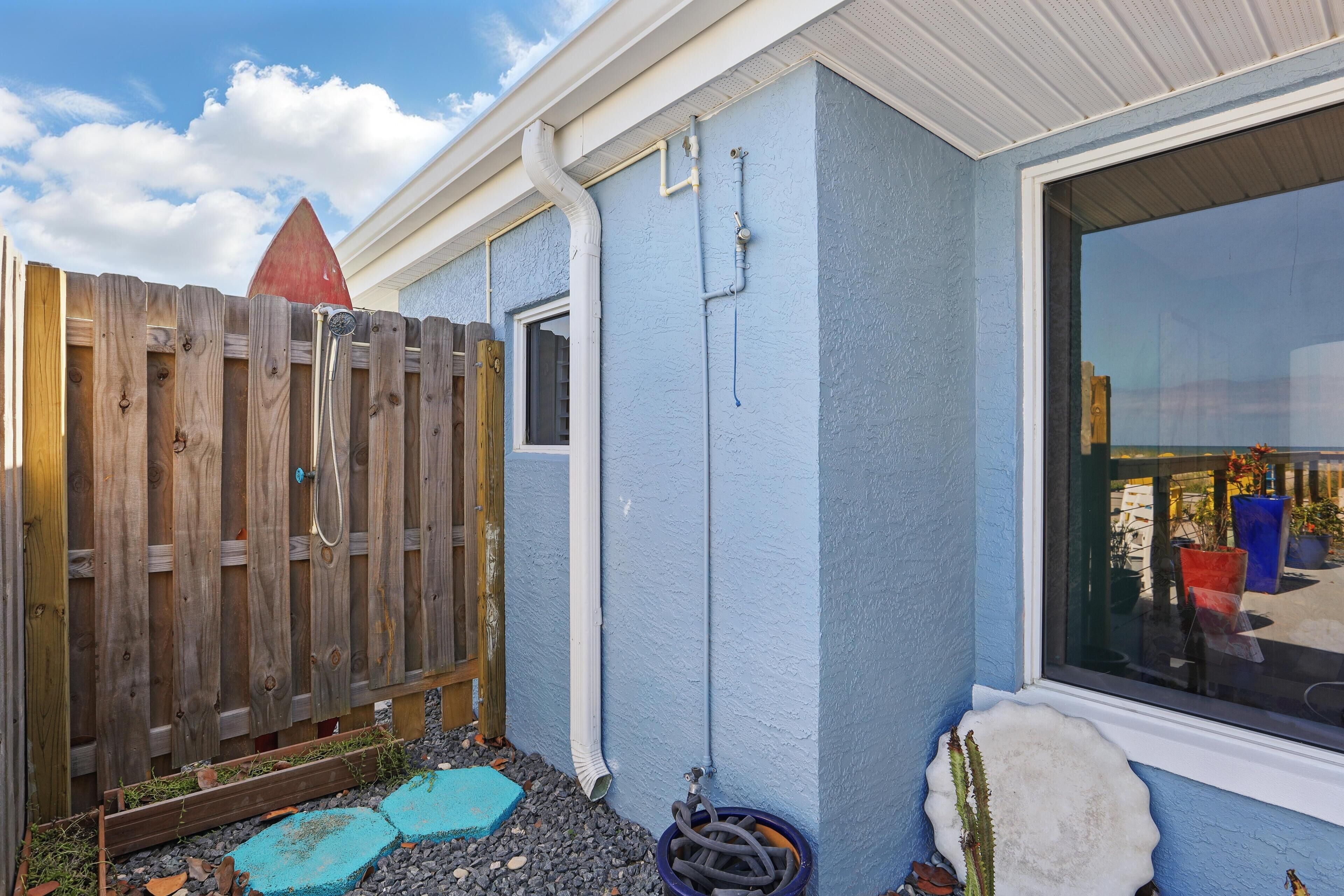 A house with a blue exterior, a wooden fence, and a window with a view of potted plants.