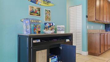 A kitchen with teal walls, wooden cabinets, and a countertop. There are several board games on a shelf, including 'Trivial Pursuit' and 'Clue'.