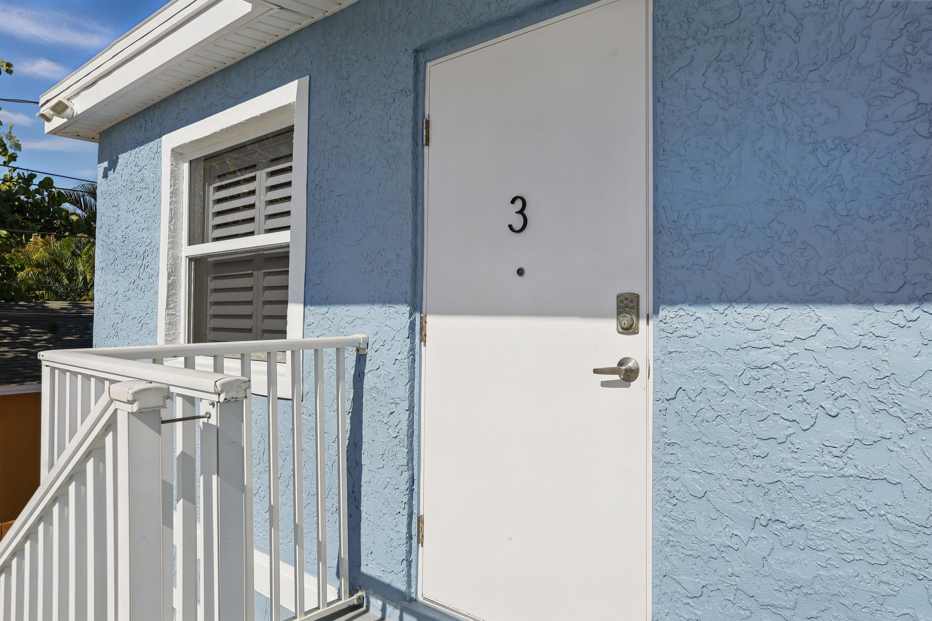 A building with a white door marked with the number 3, a white railing, and a window with shutters.