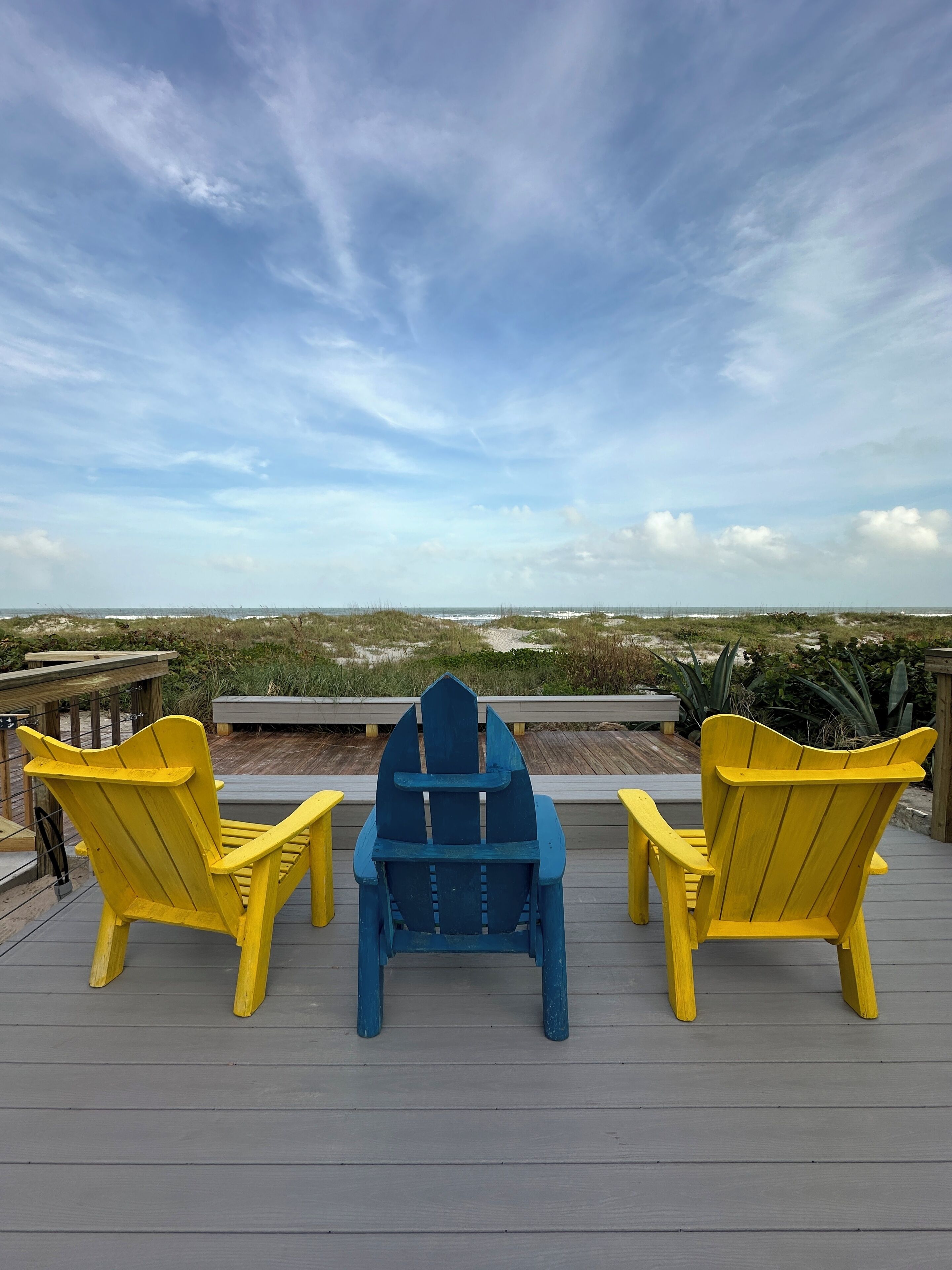 A deck with three Adirondack chairs facing a scenic view.
