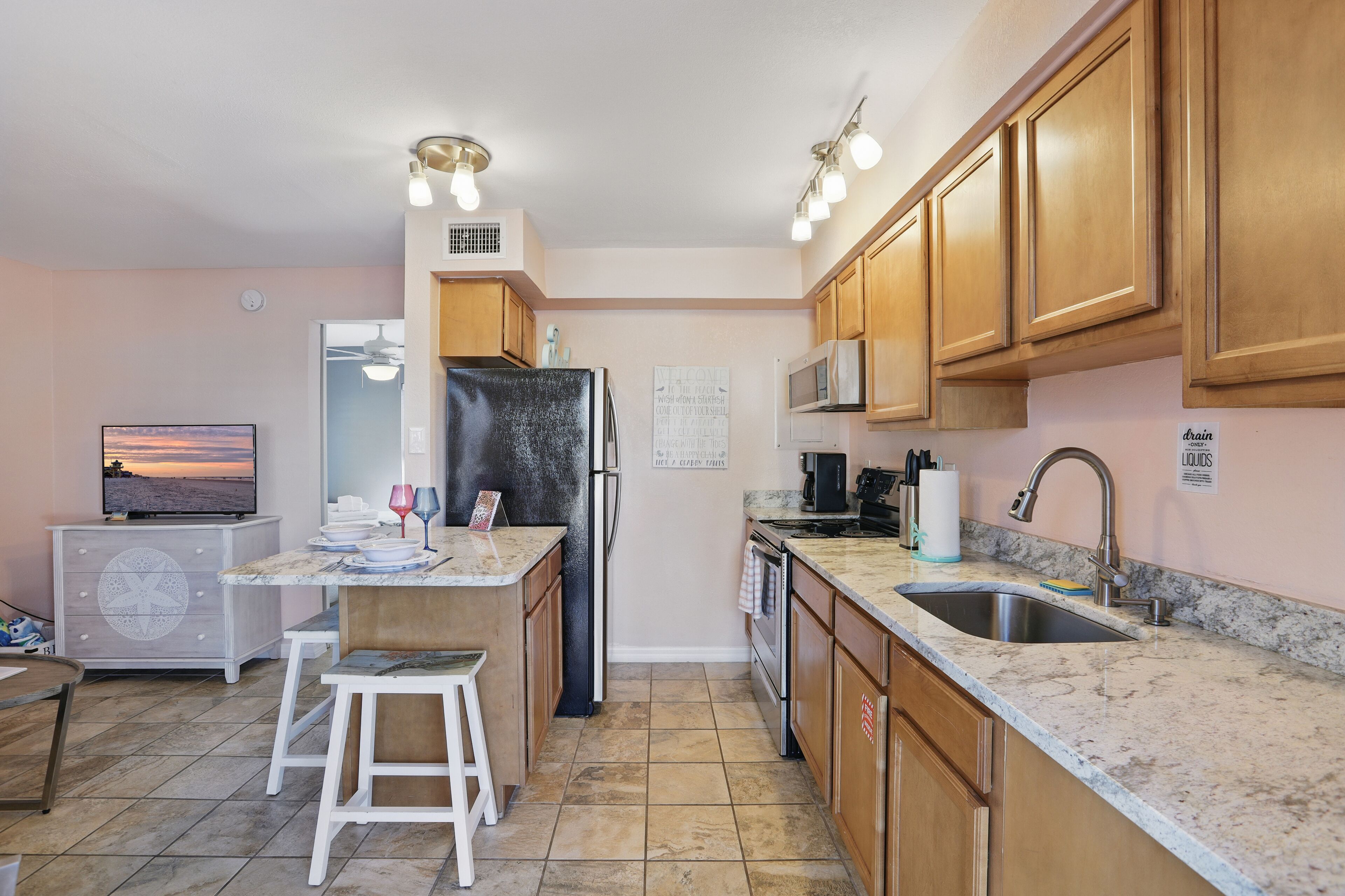 A compact kitchen with wooden cabinets, a built-in microwave, a refrigerator, and a granite countertop.