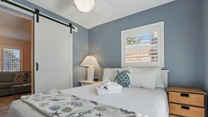 Un dormitorio con cama, mesita de noche, lámpara, ventana con persianas, sofá y puerta corredera.