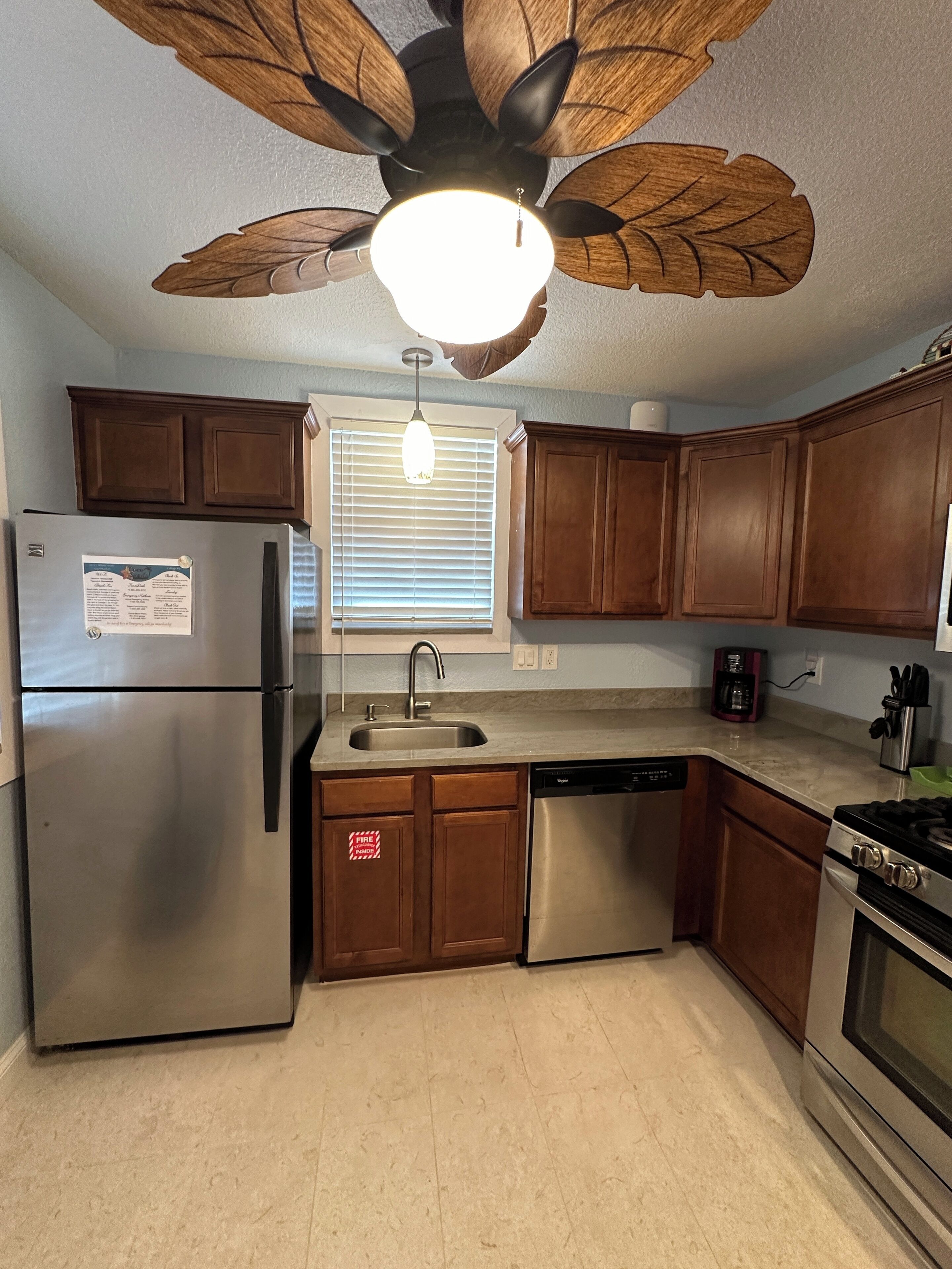 A kitchen with wooden cabinets, a stainless steel refrigerator, a dishwasher, a stove, and a ceiling fan with a light.