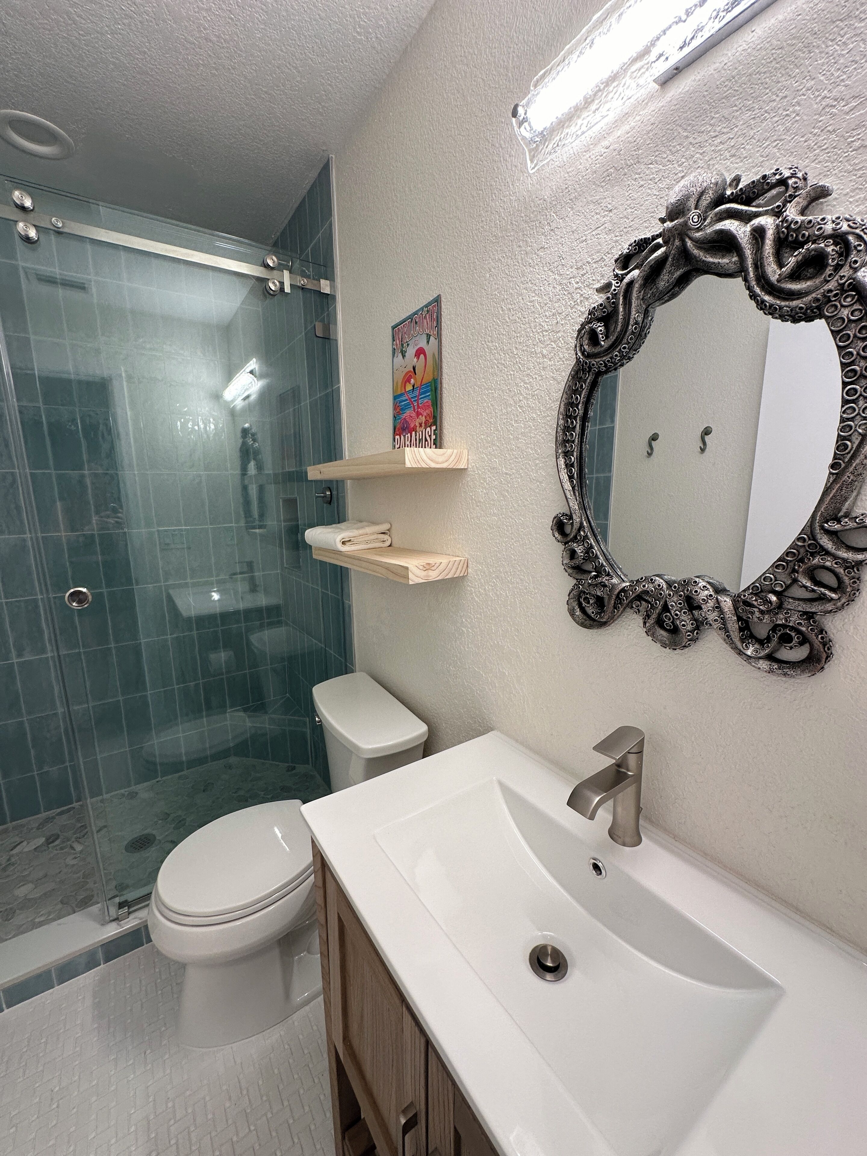 Ein Badezimmer mit Duschkabine aus Glas, Toilette, Waschbecken mit Spiegel und Handtuchhalter.
