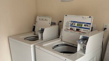 A laundry room with two washing machines, a notice sign, and a trash bin.