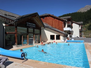 A swimming pool area with a wooden building labeled "Les Hauts de Prieaux" and a mountain in the background.