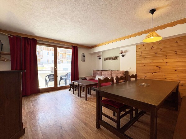 Une pièce chaleureuse avec une table à manger en bois, un canapé et une vue sur l’extérieur, accessible par une porte coulissante.
