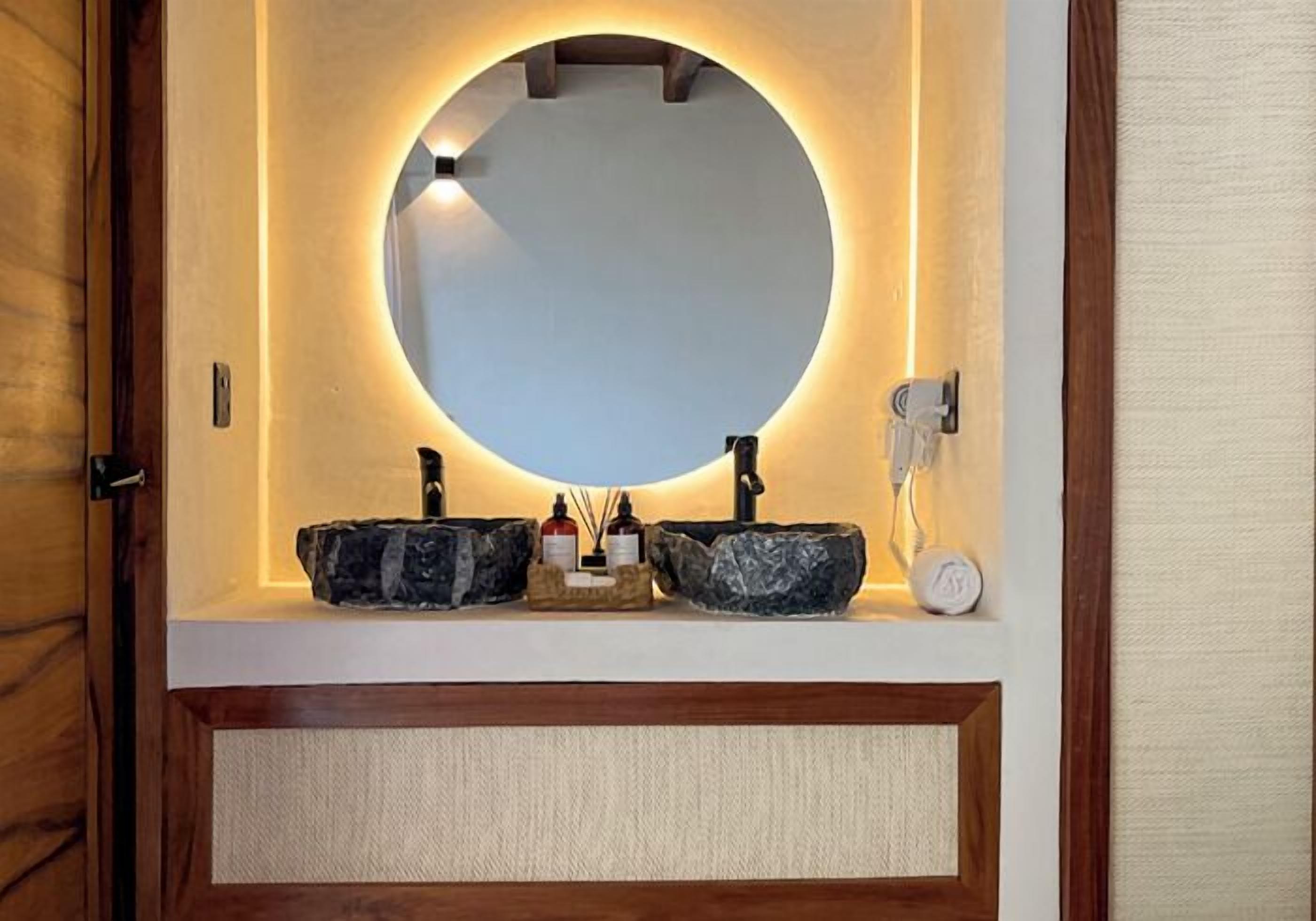 A bathroom with a round mirror, two sinks, and a telephone.