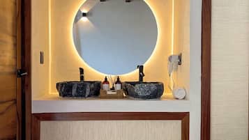 A bathroom with a round mirror, two sinks, and a telephone.