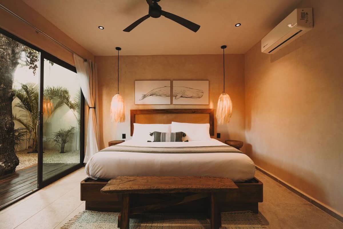 A bedroom with a large bed, two bedside tables, a ceiling fan, and a view of palm trees through a sliding glass door.