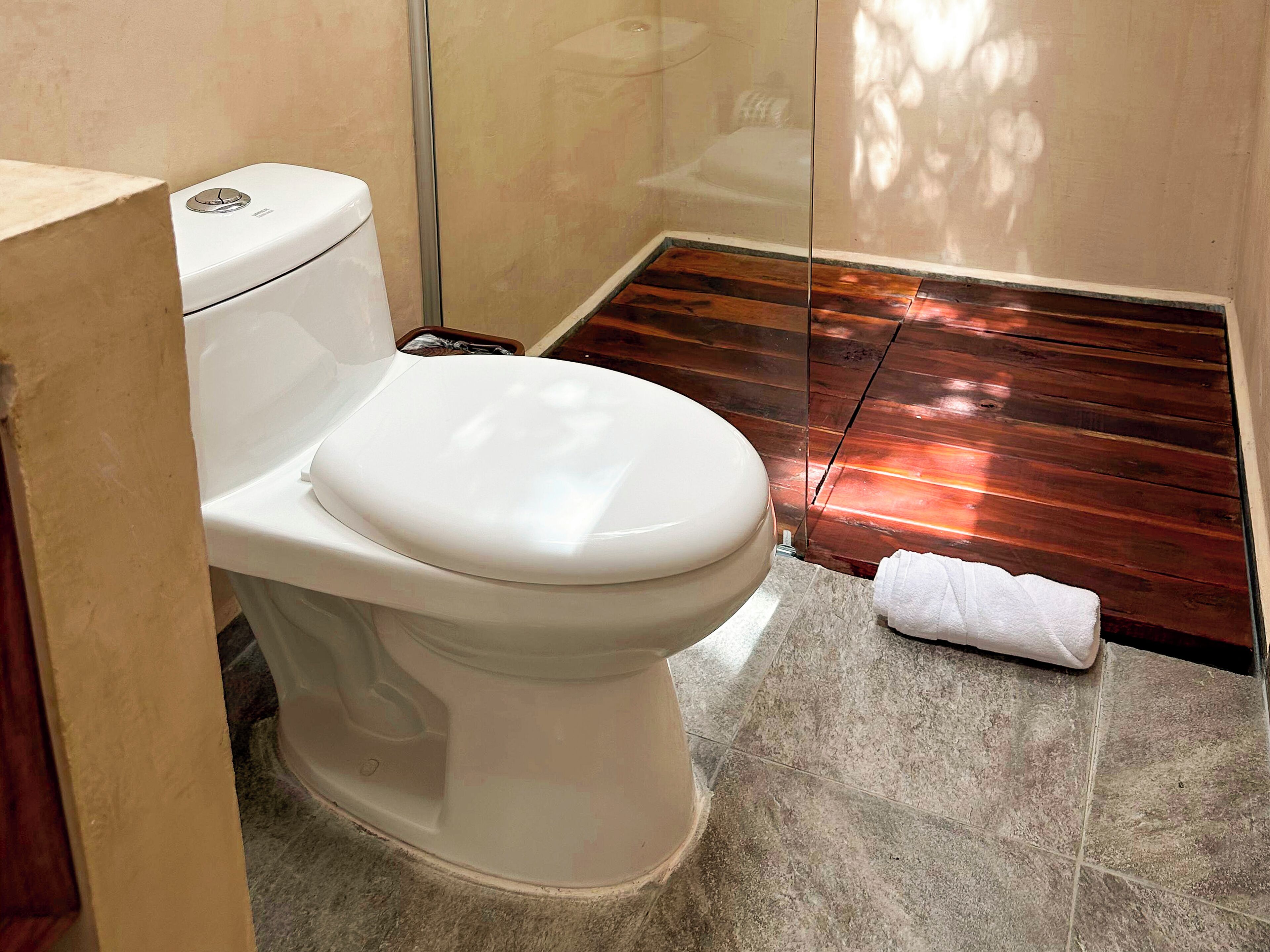 A bathroom with a white toilet, a glass shower enclosure, and a wooden floor.