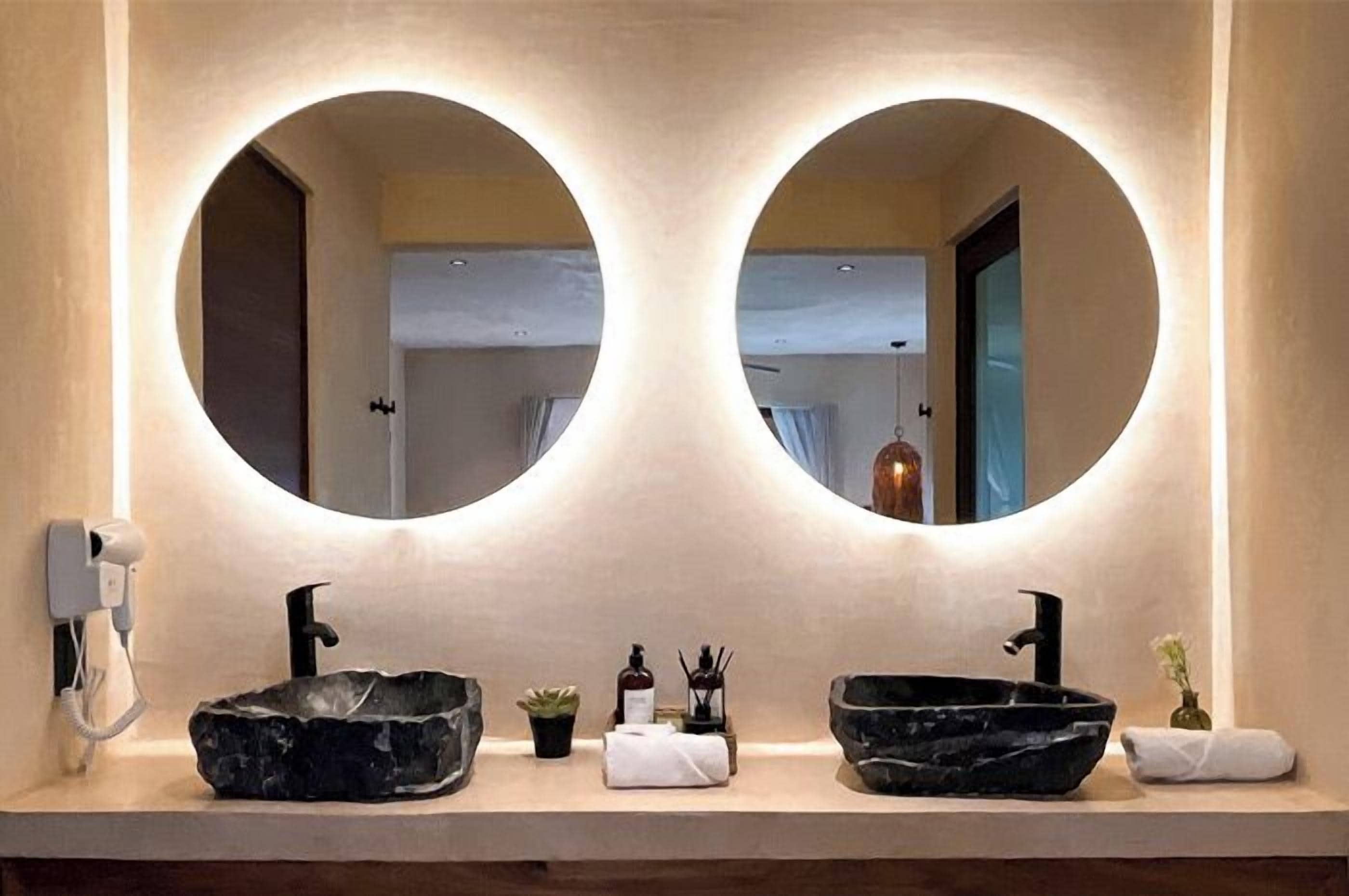 Un baño con dos espejos redondos, un lavabo negro, una toalla blanca y una planta pequeña.