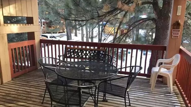 A covered outdoor area with a round metal table and chairs, a wooden deck, and a view of trees and a parked car.