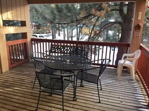 A covered outdoor area with a round metal table and chairs, a wooden deck, and a view of trees and a parked car.