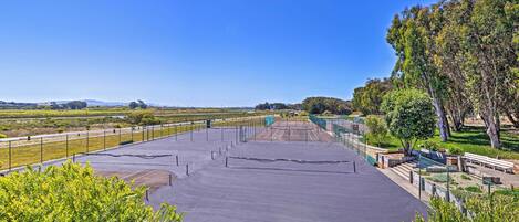 A tennis court with a net, surrounded by greenery and trees.