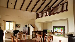 Ein geräumiges Wohnzimmer mit einem Holzessttisch und Stühlen, einer Treppe, die zu einem Balkon führt, und einem großen Gemälde an der Wand.