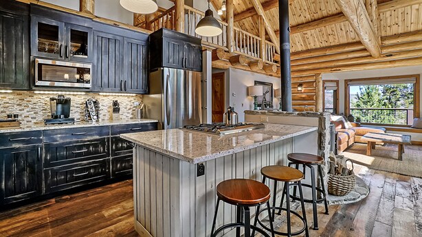 A spacious kitchen with dark cabinets, a large island with stools, and a rustic wooden ceiling.