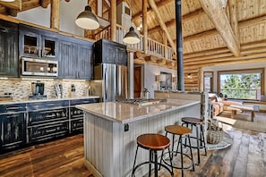 Une cuisine spacieuse avec des meubles de couleur sombre, un grand îlot central doté de tabourets et un plafond en bois rustique.
