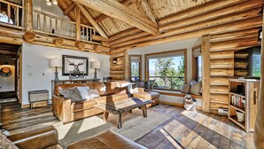 A log cabin interior with a wooden ceiling, a sofa set, a coffee table, and a bookshelf.