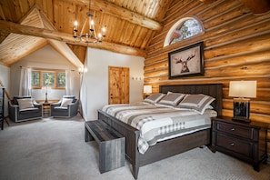 Une chambre aménagée dans un chalet en rondins, avec un grand lit, deux fauteuils, un banc et un plafond en bois.