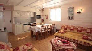 Ein gemütliches, helles Zimmer mit Esstisch, Stühlen, einer Couch und einer Küchenzeile.