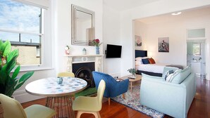 A modern living room with a fireplace, a dining area, and a bedroom with a bed and a TV.