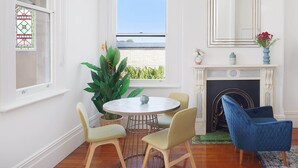 A room with a round table, two chairs, a blue armchair, a fireplace, and a large window with a view.