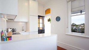 A modern kitchen with white cabinetry, a built-in island, a window with a view of the neighborhood, and a wall clock.