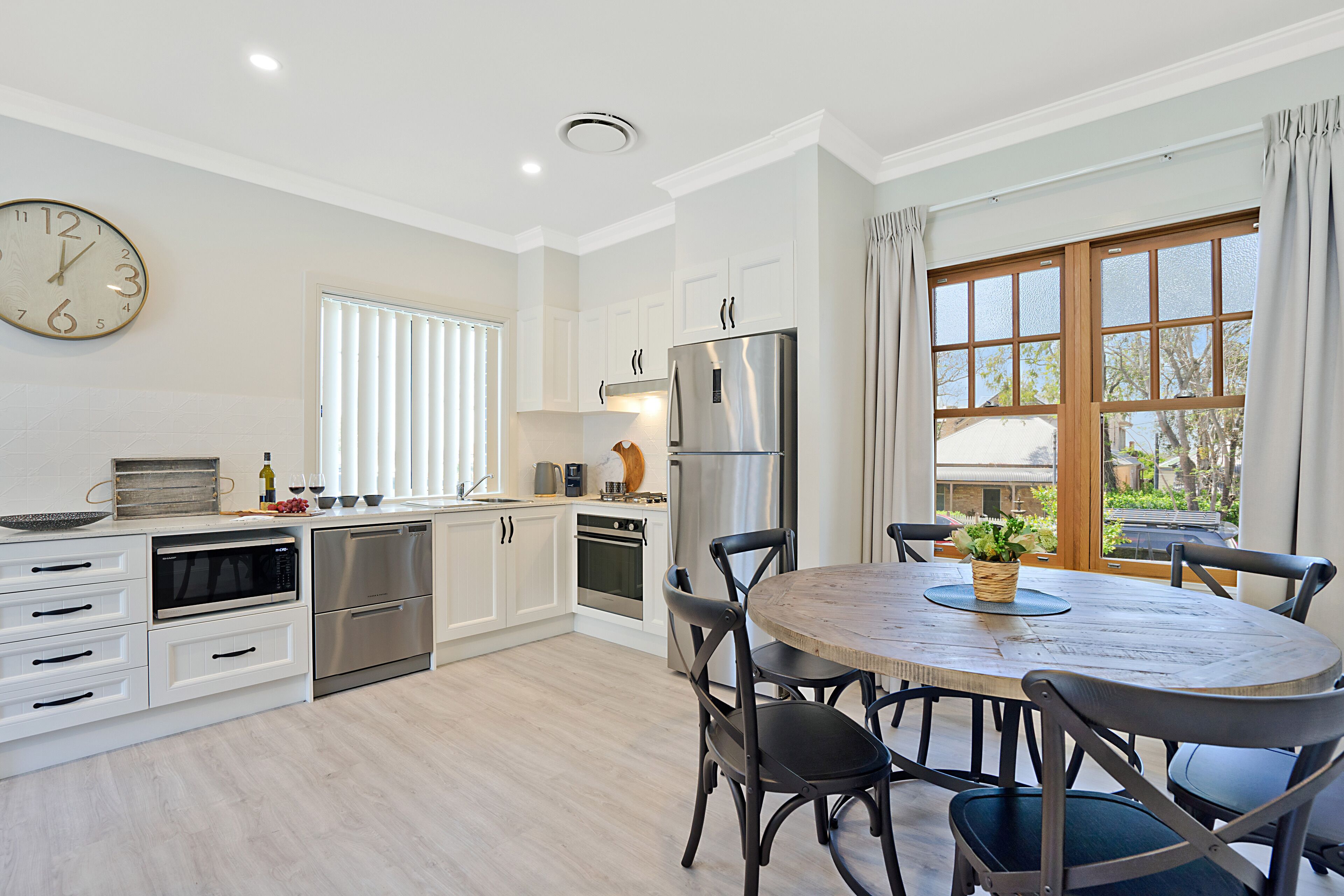 A modern kitchen with white cabinets, stainless steel appliances, and a wooden dining table with chairs.