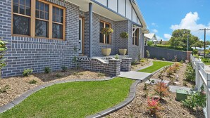 A modern two-story house with a brick exterior, large windows, and a well-maintained garden with a lawn and flower beds. - Accommodation Hunter - Adams St Maitland (Maitland)