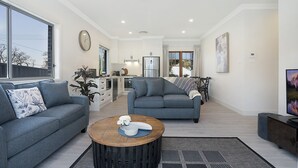 A spacious living room with a grey sofa, a wooden coffee table, and a kitchen area in the background. - Accommodation Hunter - Adams St Maitland (Maitland)