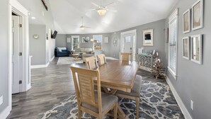 A spacious dining area with a wooden table and chairs, a ceiling fan, and a patterned rug. - The Sand Dollar is a 3BD/2BA modern home w/pool, fenced in back yard, boat parking! (Mexico Beach)