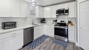 A modern kitchen with white cabinets, stainless steel appliances, and a blue patterned rug. - The Sand Dollar is a 3BD/2BA modern home w/pool, fenced in back yard, boat parking! (Mexico Beach)