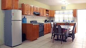 Cuina amb armaris de fusta, nevera, fogó i taula de dinar amb cadires.