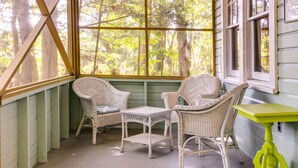 Une véranda aménagée avec des meubles en osier et une petite table, donnant sur une forêt.