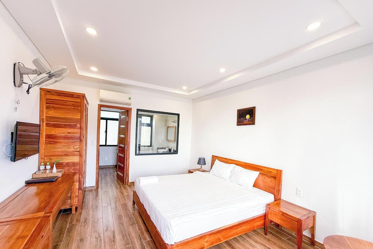 Ein Schlafzimmer mit einem hölzernen Bett, einer Holzbank, einem Nachttisch, einem Spiegel und einem Deckenventilator.