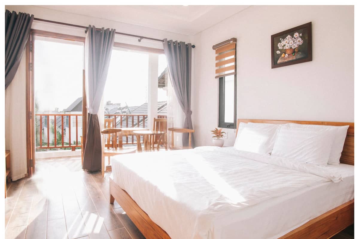 Ein Schlafzimmer mit einem Holzbett, einem Balkon mit Holzstühlen und einem Fenster mit Vorhängen.