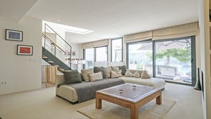 A modern living room with a sofa, coffee table, and a staircase leading to a balcony. - Noelia: Exclusive villa overlooking the sea and private pool. (L'Escala)