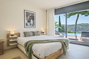 Ein Schlafzimmer mit einem großen Bett, zwei Nachttischen inklusive Lampen, einem gerahmten Bild an der Wand und Blick auf Pool und Landschaft.